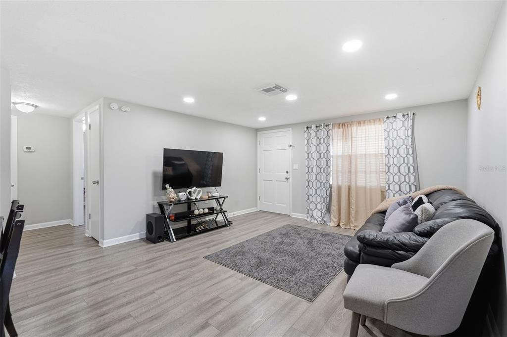 A living room features light gray walls, wood-look flooring, a television, and a leather sofa — 9825 LAKESIDE LANE, PORT RICHEY, FL
