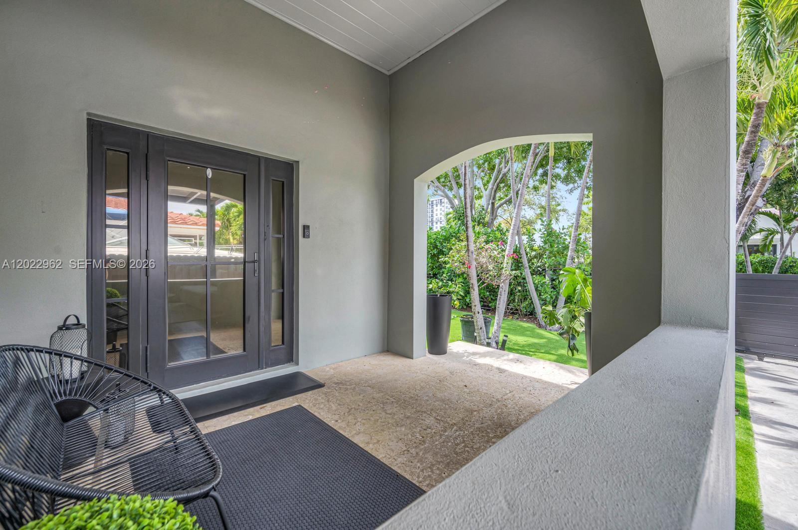 A covered patio features a dark-framed glass door, stone flooring, and a black metal chair — 1852 SW 10th St, Miami FL 33135, MIAMI, FL