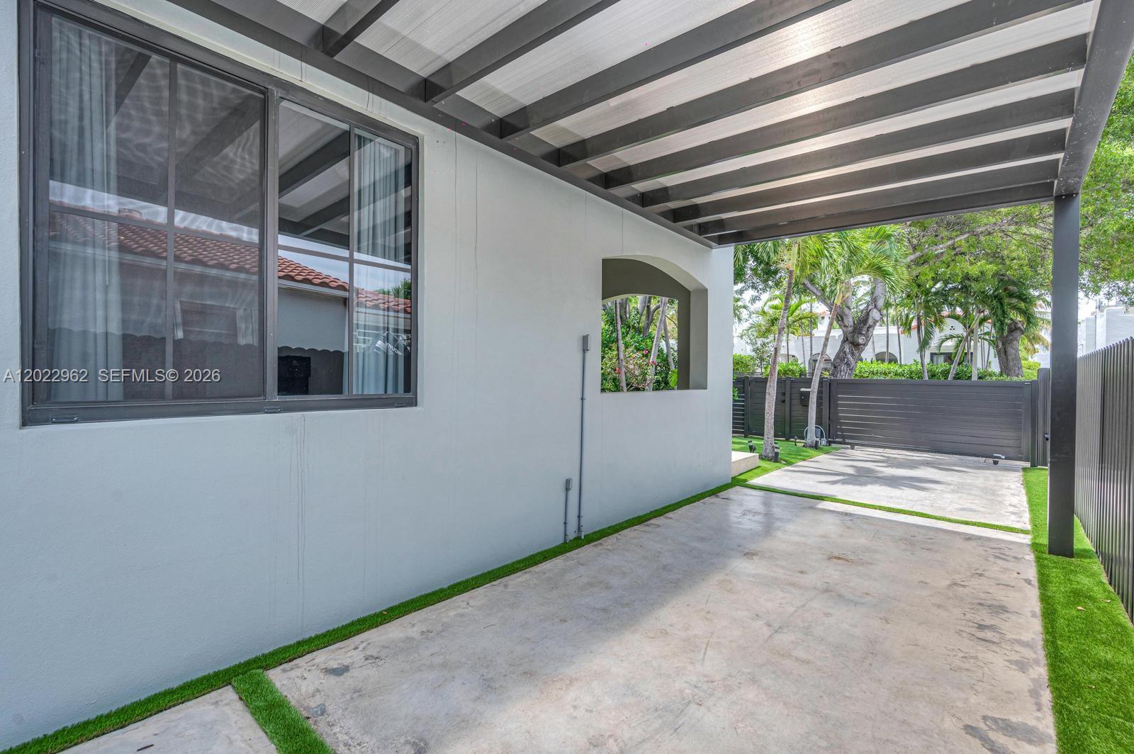 A concrete driveway leads to a covered patio area beside a gray exterior wall — 1852 SW 10th St, Miami FL 33135, MIAMI, FL