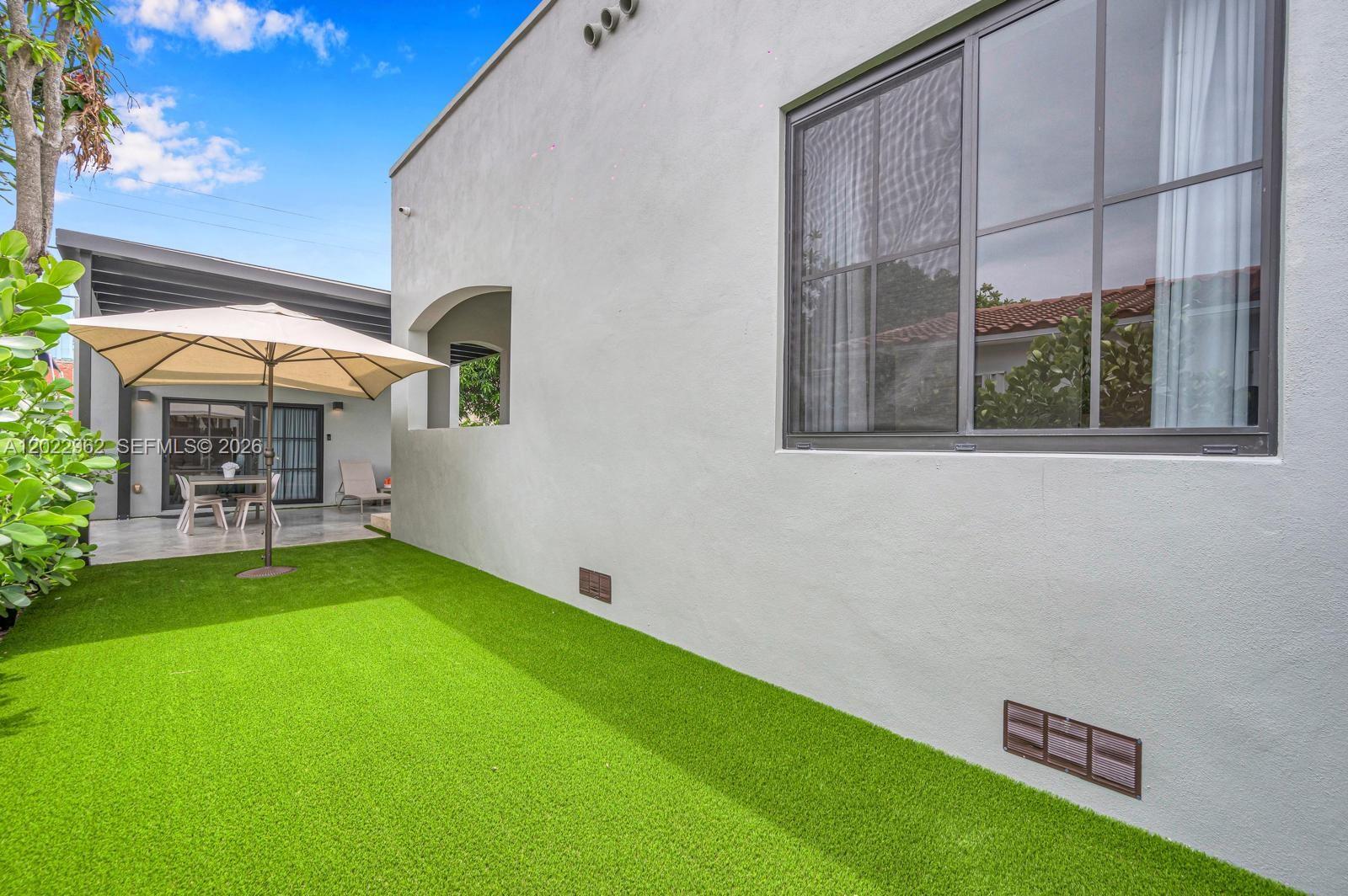 A backyard features artificial turf, a beige patio umbrella, and a light-colored stucco exterior wall — 1852 SW 10th St, Miami FL 33135, MIAMI, FL