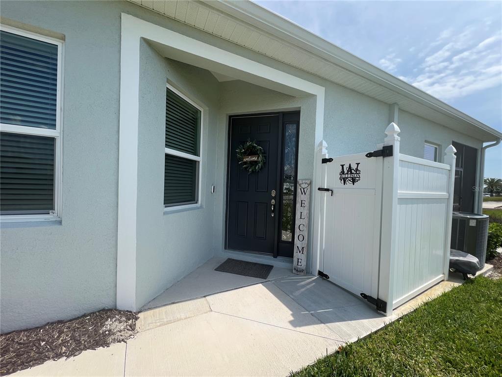 The exterior of a house features a covered entryway with a dark door and white fence — 1867 NOTTINGHAM TRAIL, PORT CHARLOTTE, FL