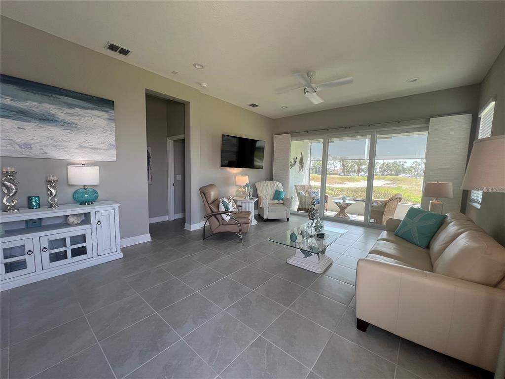 A living room features tile flooring, a beige sofa, and large sliding glass doors — 1867 NOTTINGHAM TRAIL, PORT CHARLOTTE, FL