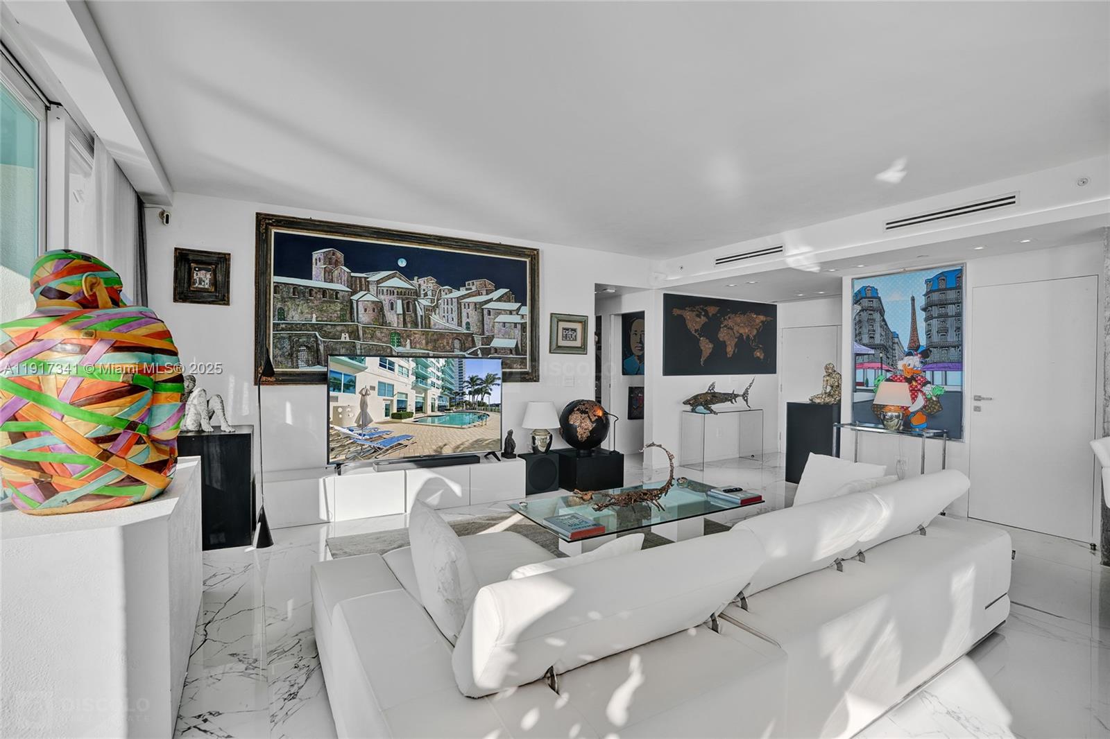 A modern living room features white marble floors, a large sectional sofa, and colorful artwork — 650 West Ave, Miami Beach FL 33139, MIAMI BEACH, FL