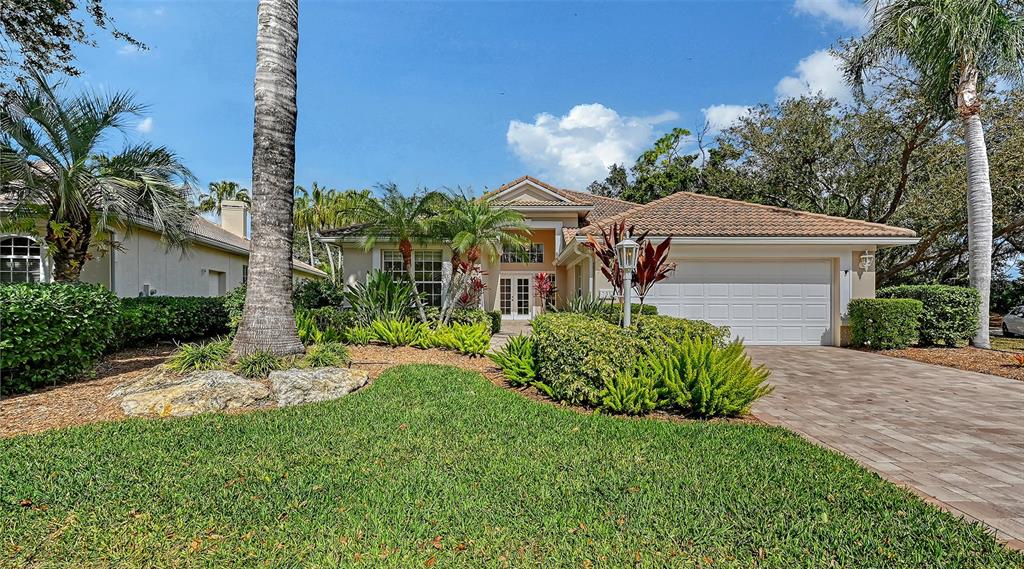 A single-story house with a beige stucco exterior, a tiled roof, and a paved driveway — 7318 WINDEMERE LANE, UNIVERSITY PARK, FL