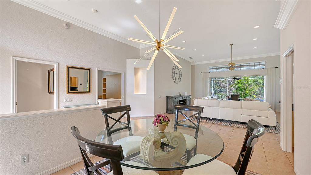 A dining area with a glass table and modern chandelier opens into a living room — 7318 WINDEMERE LANE, UNIVERSITY PARK, FL