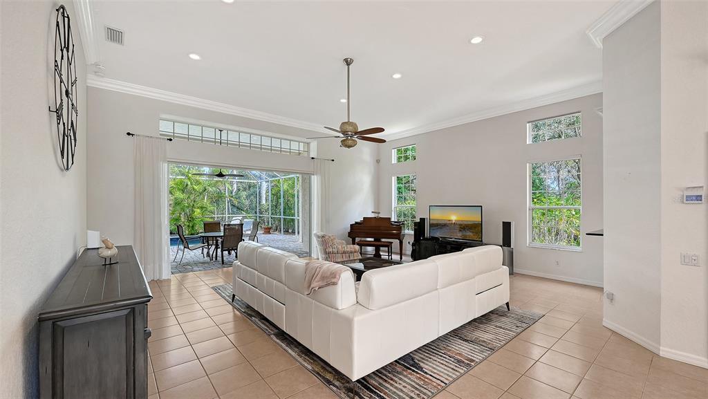 A spacious living room features a white sectional sofa, a piano, and sliding glass doors — 7318 WINDEMERE LANE, UNIVERSITY PARK, FL