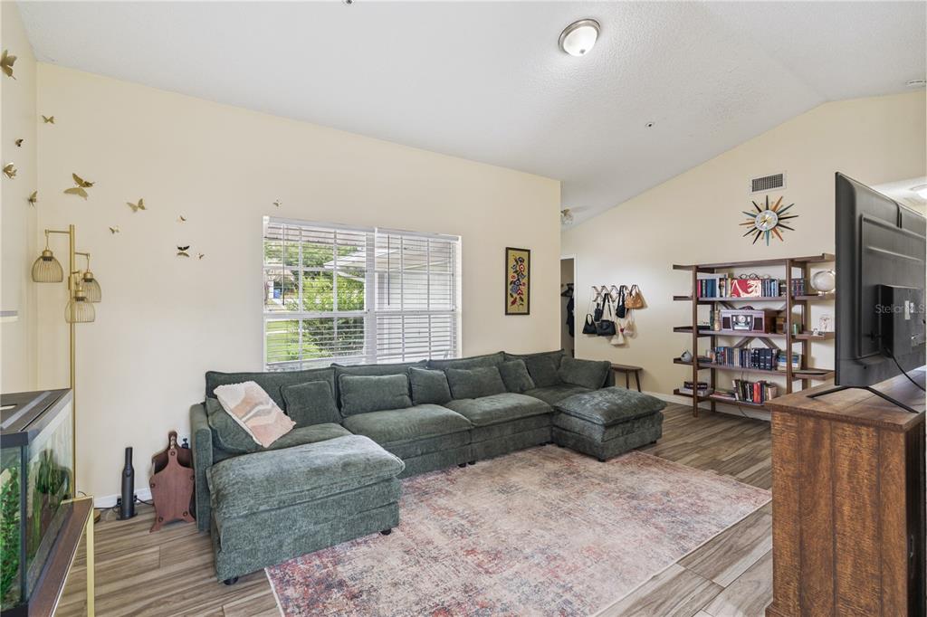 A living room features a large green sectional sofa, a patterned rug, and a bookshelf — 808 ORANGE BROOK DRIVE, MINNEOLA, FL