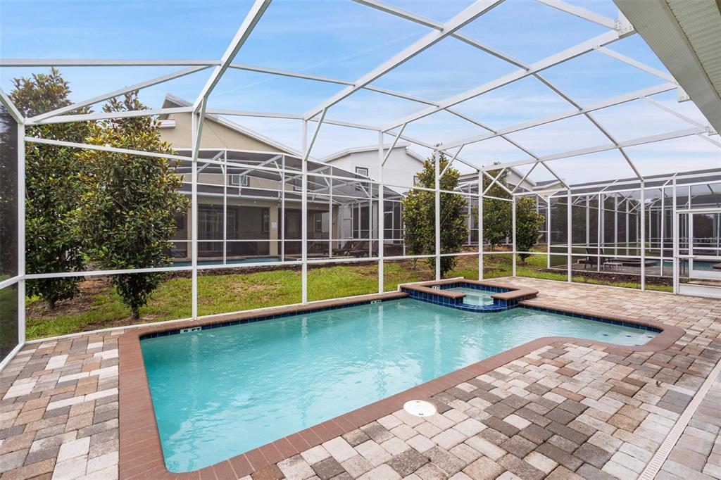 A screened-in patio features a swimming pool with an attached spa and paver decking — 870 DROP SHOT DRIVE, DAVENPORT, FL