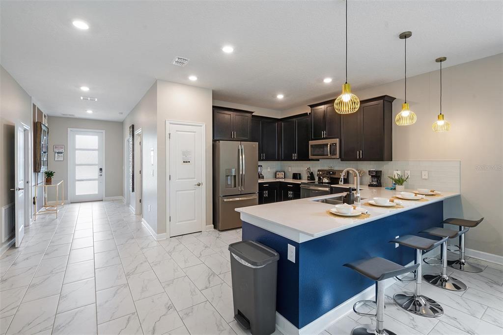 A modern kitchen features dark cabinets, stainless steel appliances, a blue island, and white tile floors — 870 DROP SHOT DRIVE, DAVENPORT, FL