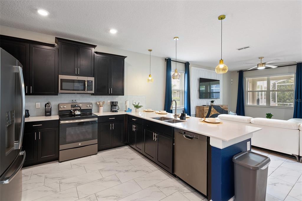 A kitchen with dark cabinets, white countertops, stainless steel appliances, and light-colored tile flooring — 870 DROP SHOT DRIVE, DAVENPORT, FL