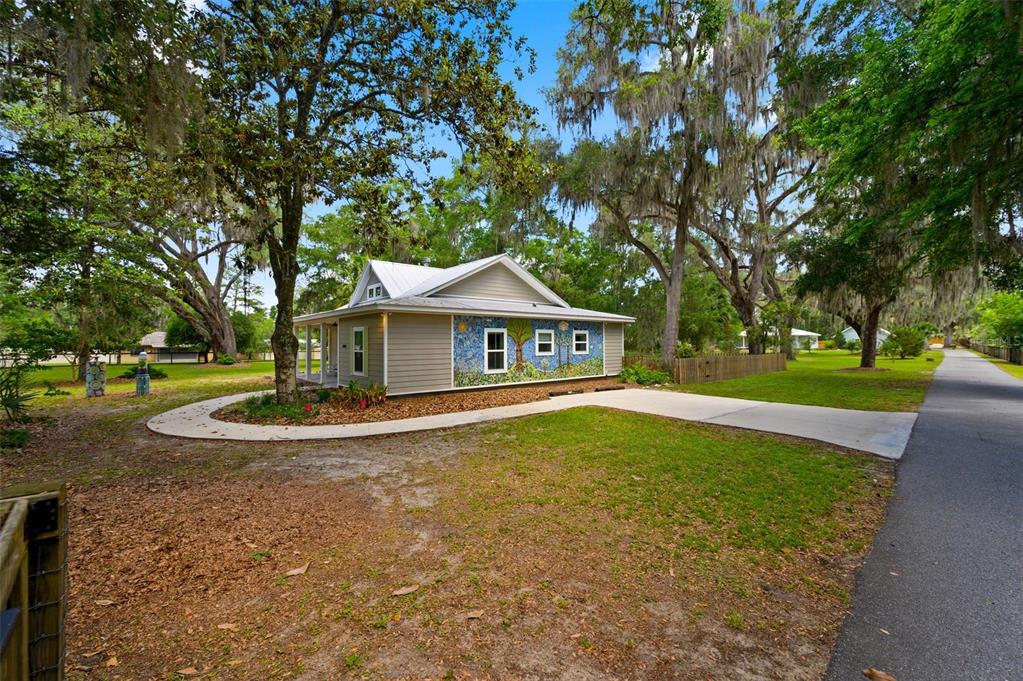 A tan house with a mosaic mural on its side sits among trees near a road — 2620 NW 31ST AVENUE, GAINESVILLE, FL