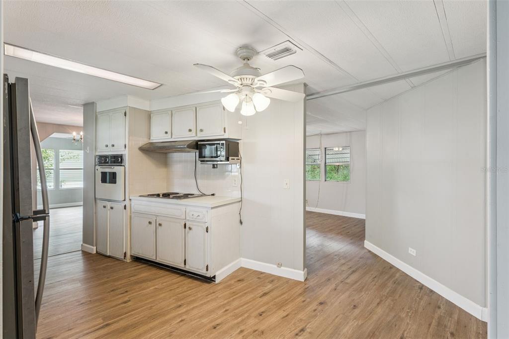 A kitchen with white cabinets, a wall oven, and wood-look flooring opens to another room — 16842 ELDERBERRY DRIVE, MONTVERDE, FL