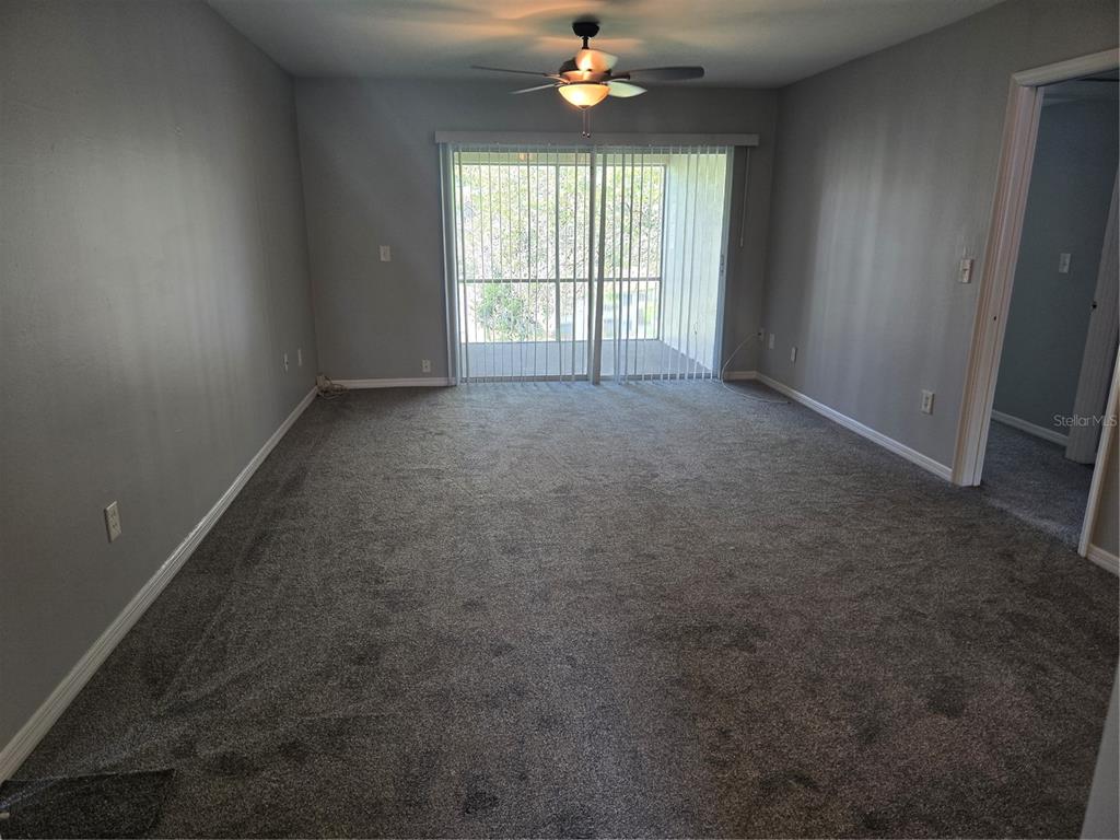 An empty living room features gray walls, gray carpeting, a ceiling fan, and sliding glass doors — 10342 CARROLLWOOD LANE UNIT 168, TAMPA, FL