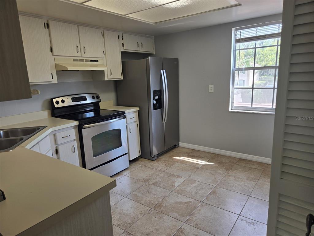 A kitchen features white cabinets, stainless steel appliances, tile flooring, and a window — 10342 CARROLLWOOD LANE UNIT 168, TAMPA, FL