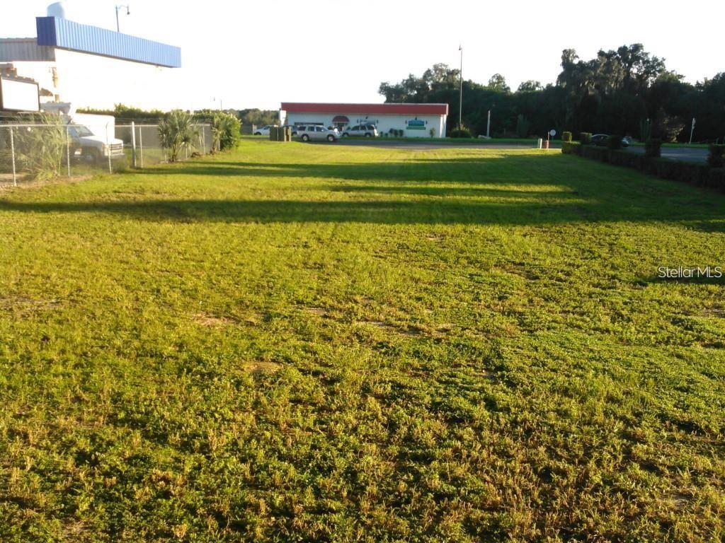 A grassy, vacant lot is shown with a chain-link fence and a distant commercial building — E. NORTH BLVD (US HWY 441), LEESBURG, FL