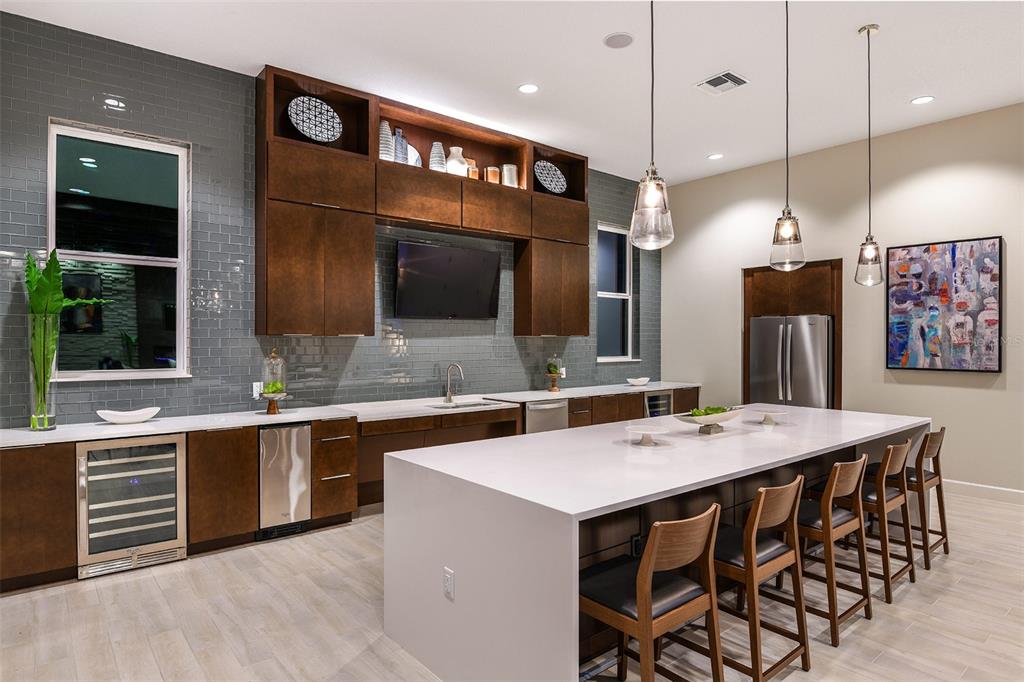 A modern kitchen features dark wood cabinetry, a large white island, and gray tile walls — 7545 LAUREATE BLVD UNIT 7208, ORLANDO, FL