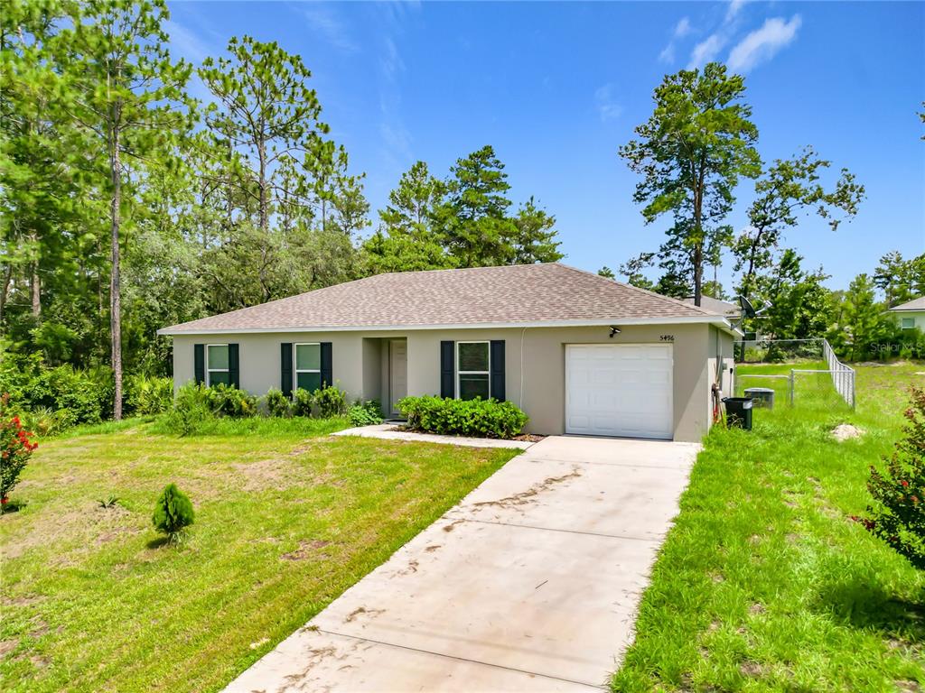 A single-story house with a beige exterior, a white garage door, and a concrete driveway — 5496 SW 153RD STREET ROAD, OCALA, FL