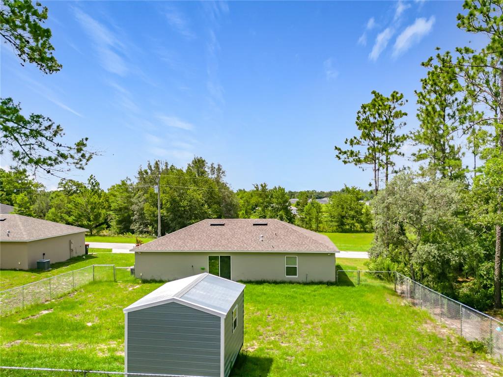 A backyard view of a house with a shed, a chain-link fence, and trees — 5496 SW 153RD STREET ROAD, OCALA, FL