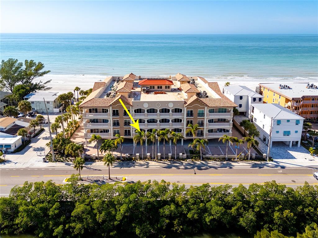 An aerial view of a multi-story beachfront condominium building with palm trees and a road — 604 GULF BOULEVARD UNIT 207, INDIAN ROCKS BEACH, FL
