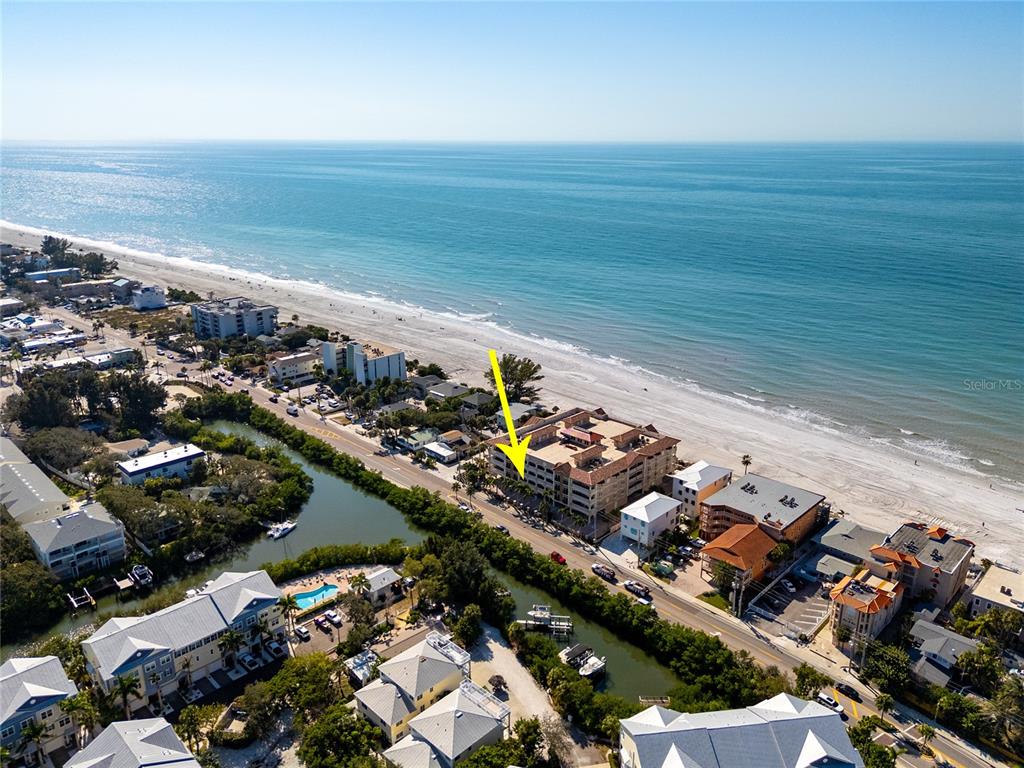 An aerial view shows a multi-story beachfront condominium building indicated by a yellow arrow — 604 GULF BOULEVARD UNIT 207, INDIAN ROCKS BEACH, FL
