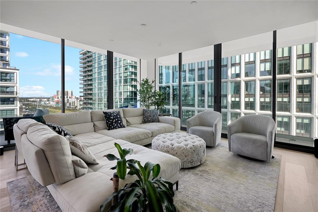 A modern living room features a large sectional sofa, two armchairs, and floor-to-ceiling windows — 1000 WATER STREET UNIT 1002, TAMPA, FL