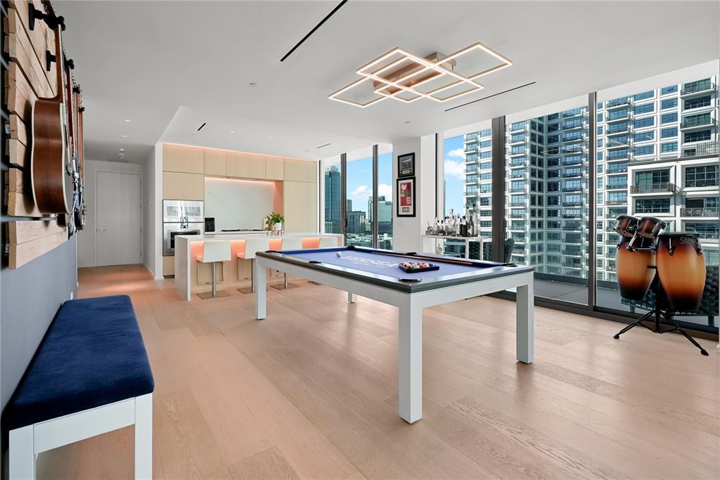 A modern game room features a pool table, kitchen island, and floor-to-ceiling windows overlooking city buildings — 1000 WATER STREET UNIT 1002, TAMPA, FL