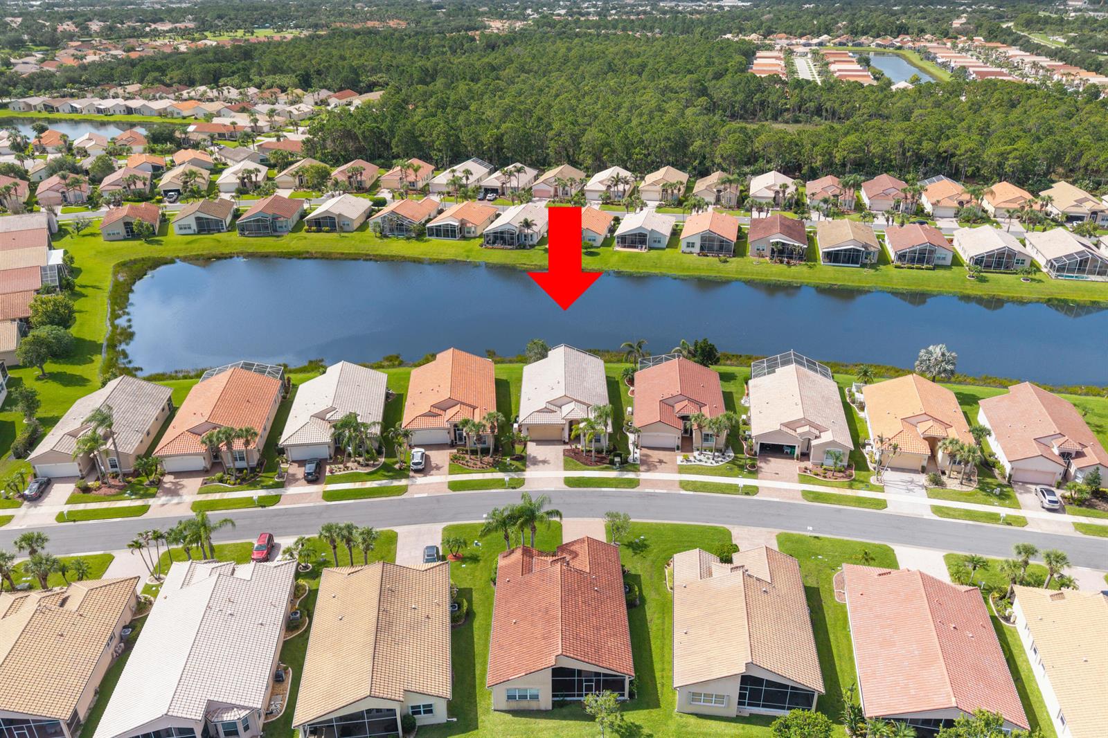 An aerial view shows a suburban neighborhood with houses bordering a central lake — 396 NW SPRINGVIEW Loop, Port St. Lucie FL 34986, PORT ST. LUCIE, FL