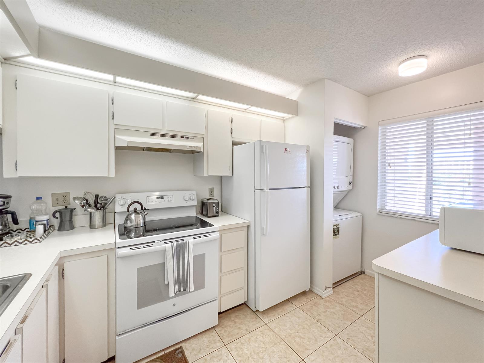 A white kitchen features a stove, refrigerator, stacked laundry unit, and tile flooring — 353 S Us Highway 1 # B309, Jupiter FL 33477, JUPITER, FL