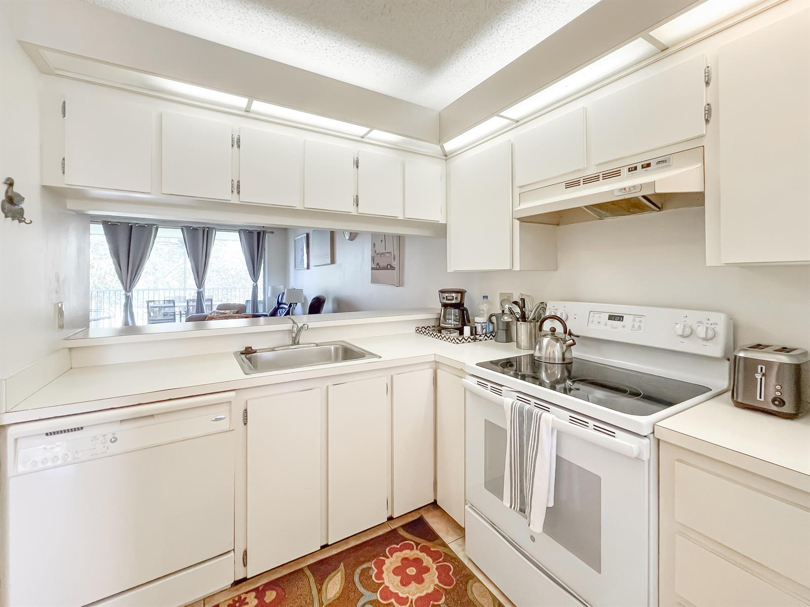 A white kitchen features a dishwasher, electric range, sink, and a pass-through window — 353 S Us Highway 1 # B309, Jupiter FL 33477, JUPITER, FL