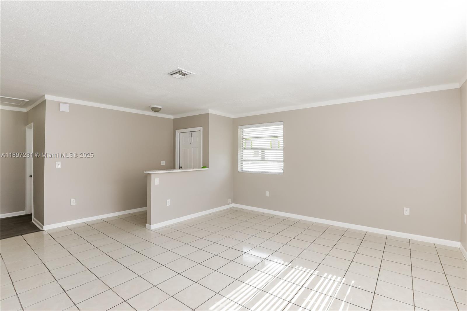 An empty room features beige walls, white crown molding, and light-colored square floor tiles — 381 NE 164th St # 0, Miami FL 33162, MIAMI, FL