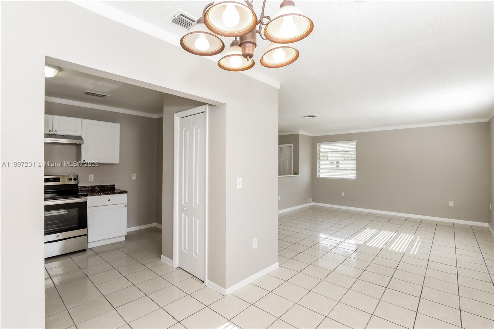 A kitchen with white cabinets and stainless steel appliances opens into a tiled living area — 381 NE 164th St # 0, Miami FL 33162, MIAMI, FL