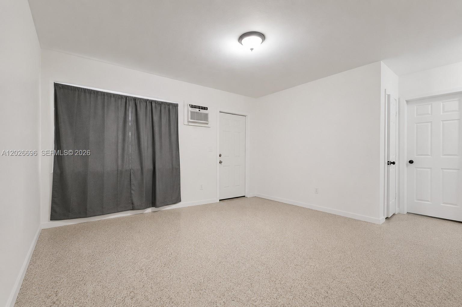 This room features white walls, beige carpet, a window with gray curtains, and two doors — 69 NW 5th St, Homestead FL 33030, HOMESTEAD, FL