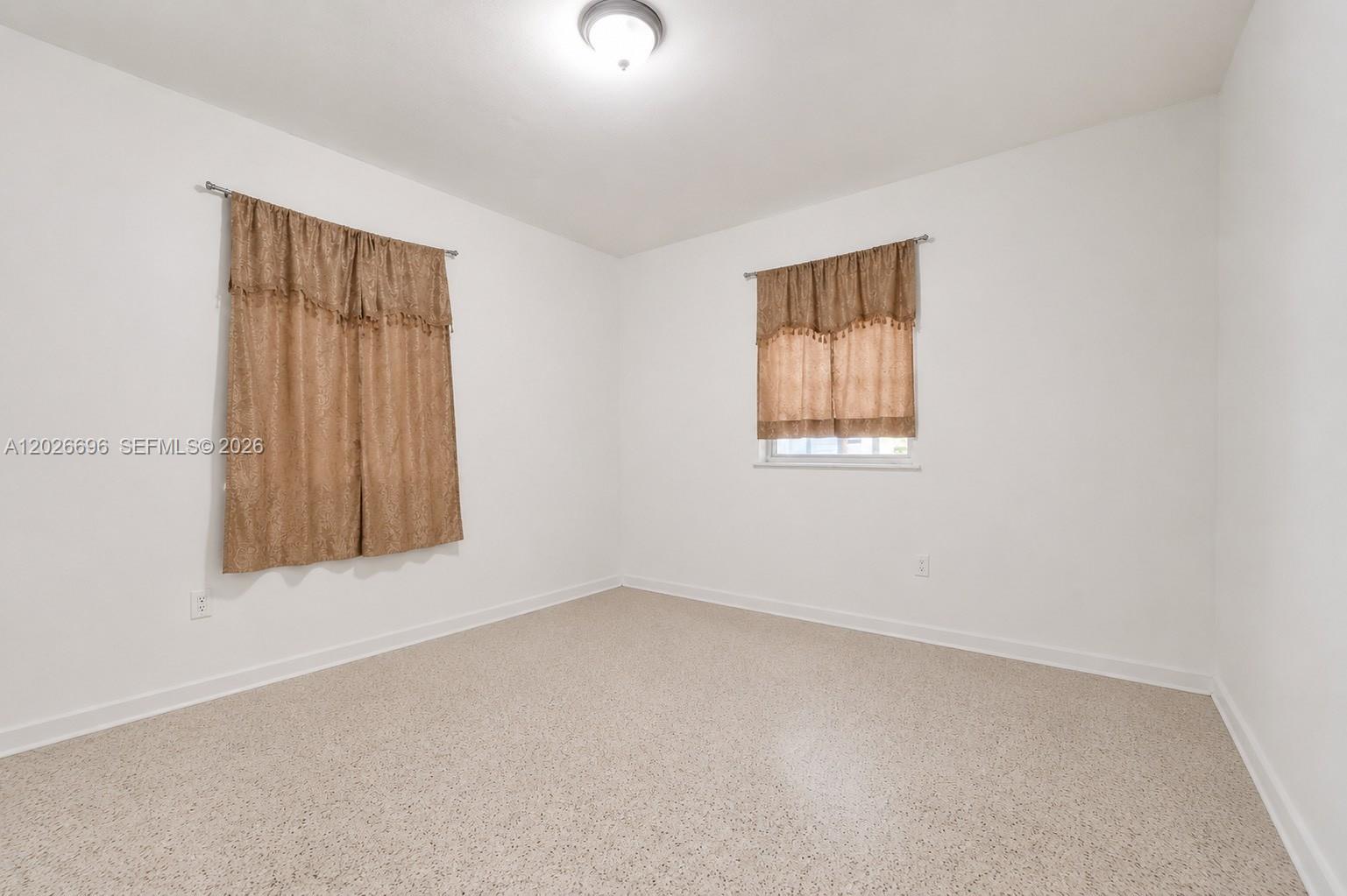 An empty bedroom features white walls, a light-colored speckled floor, and two windows with curtains — 69 NW 5th St, Homestead FL 33030, HOMESTEAD, FL