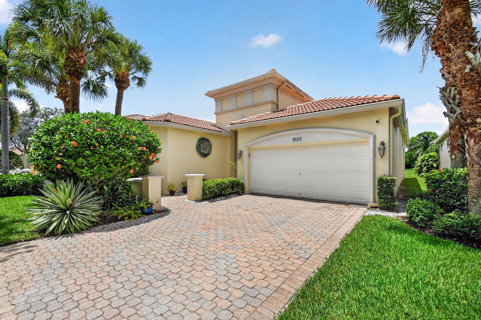 A single-story house with a paved driveway, a two-car garage, and surrounding palm trees — 8553 E Via Grande E, Wellington FL 33411, WELLINGTON, FL
