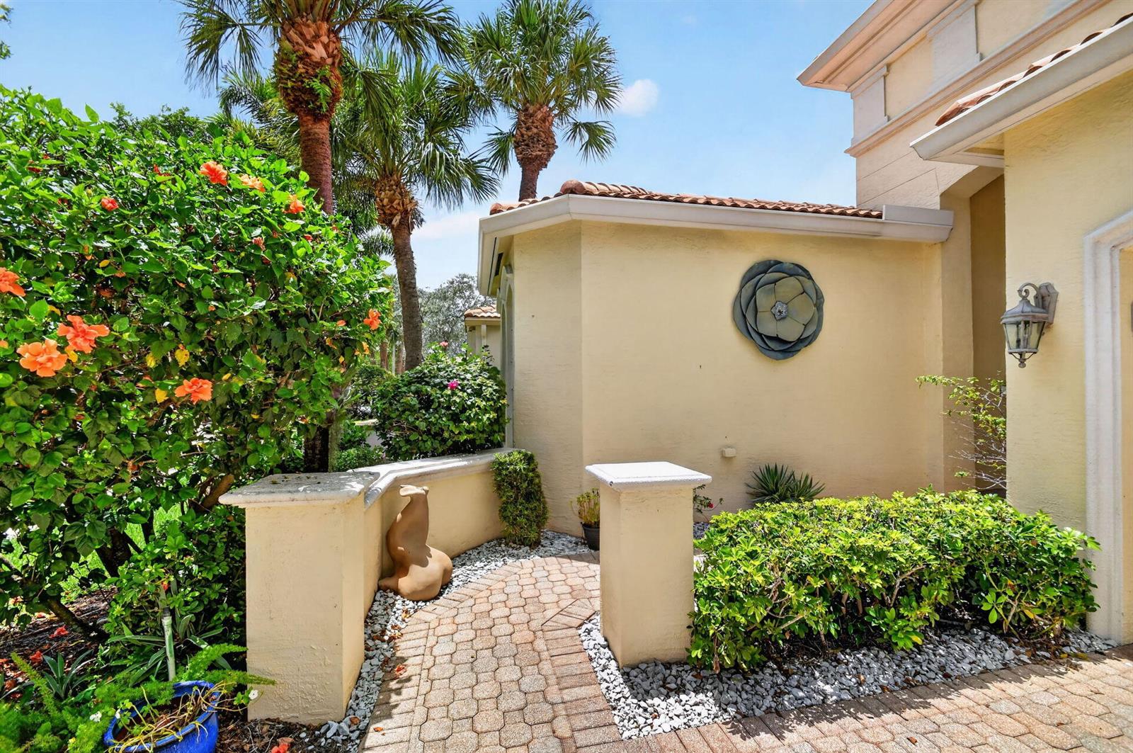 A paved walkway leads to the entrance of a house with a decorative wall ornament — 8553 E Via Grande E, Wellington FL 33411, WELLINGTON, FL