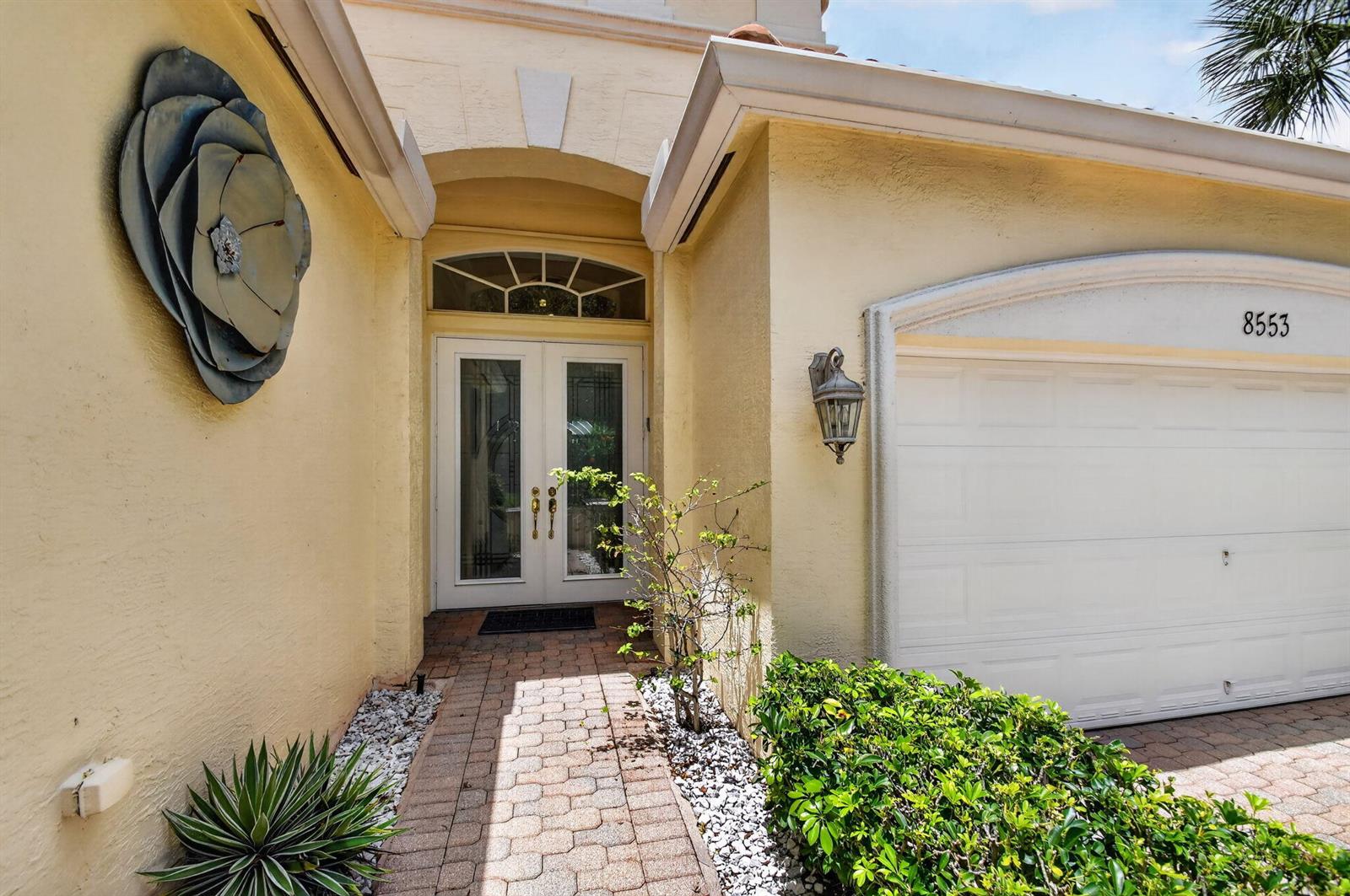 A yellow stucco house exterior features a double front door, a garage, and landscaping — 8553 E Via Grande E, Wellington FL 33411, WELLINGTON, FL