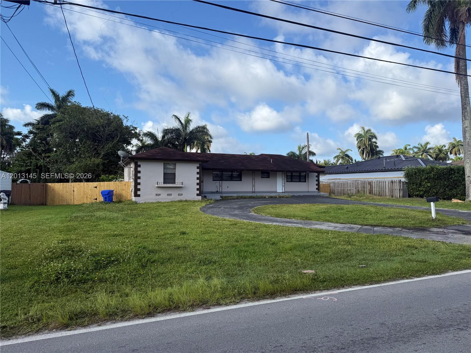 A single-story house with a curved driveway and a fenced yard under a cloudy sky — 2830 Johnson St # 1, Hollywood FL 33020, HOLLYWOOD, FL