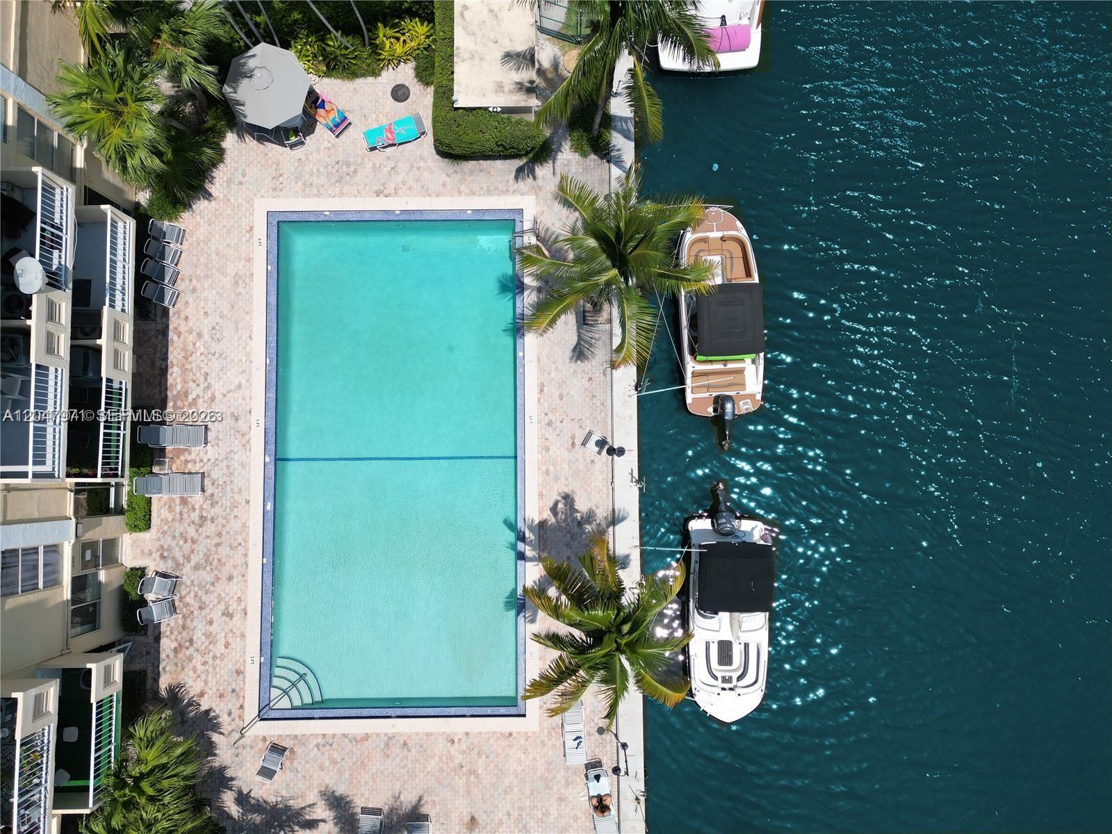 An aerial view shows a rectangular swimming pool next to a canal with docked boats — 2350 NE 135th St # 403, North Miami FL 33181, NORTH MIAMI, FL