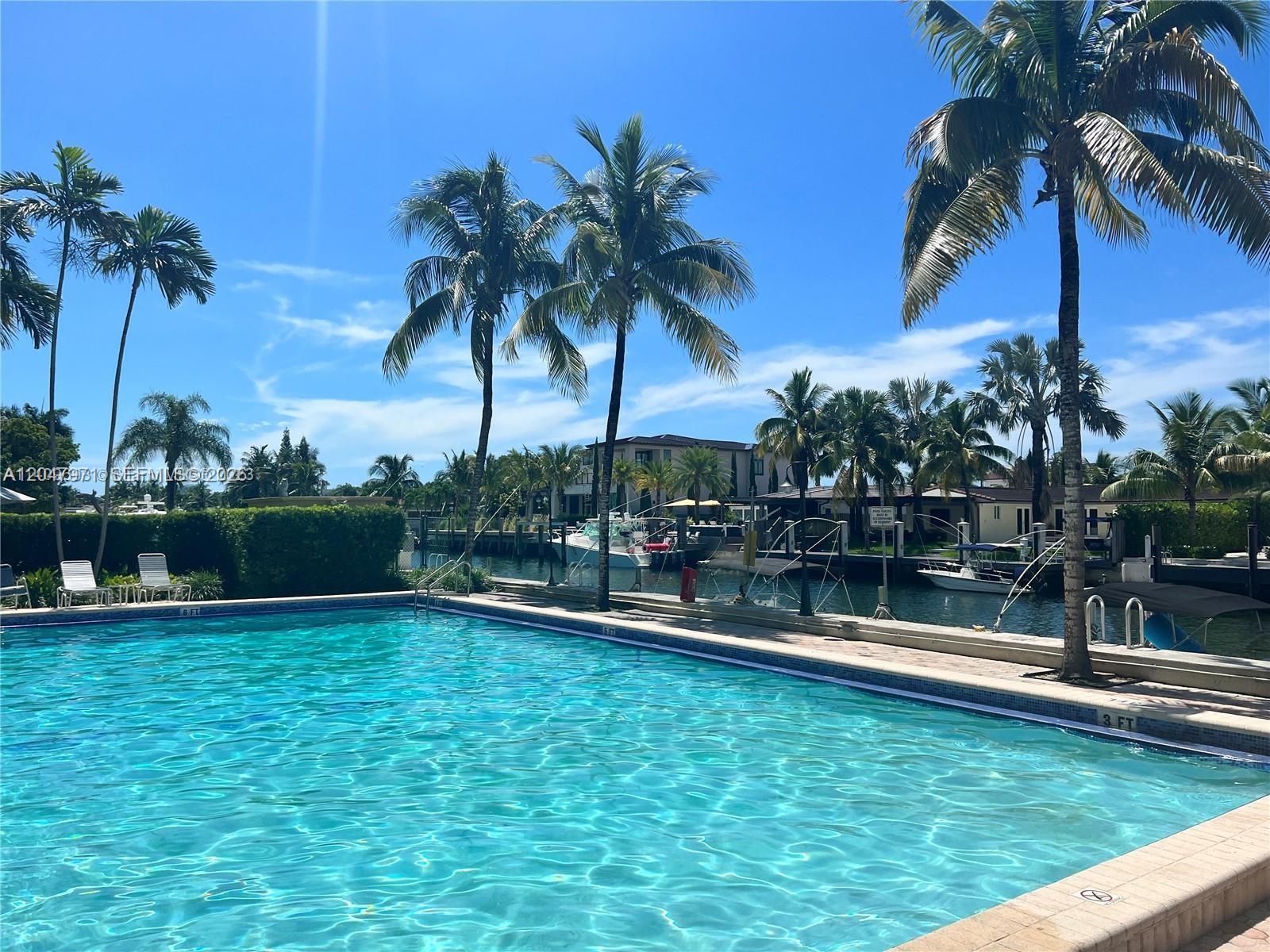 A swimming pool overlooks a canal with docked boats and palm trees under a blue sky — 2350 NE 135th St # 403, North Miami FL 33181, NORTH MIAMI, FL
