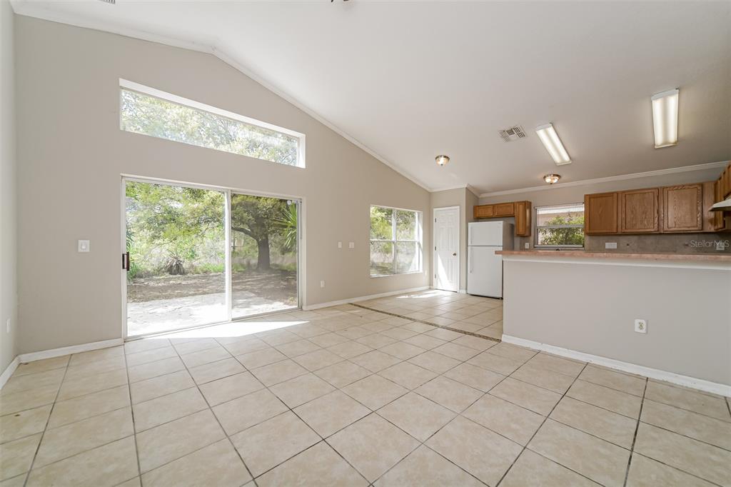 An open-concept living area with vaulted ceilings, tile flooring, and a kitchen with wooden cabinets — 948 CHANLER DRIVE, HAINES CITY, FL