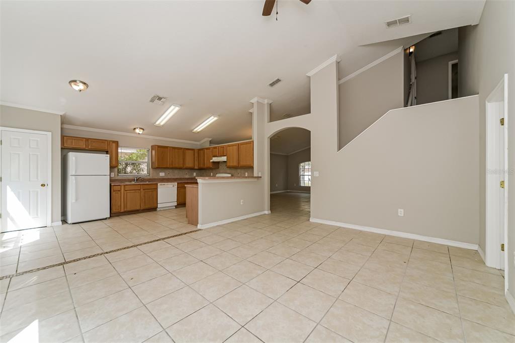 An open-concept kitchen with wood cabinets and tile flooring overlooks a spacious living area — 948 CHANLER DRIVE, HAINES CITY, FL