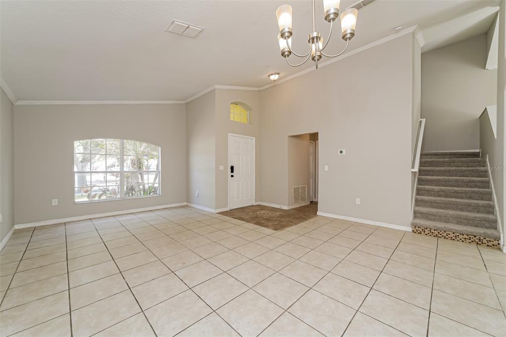 An open-concept living area features light tile flooring, a chandelier, and a carpeted staircase — 948 CHANLER DRIVE, HAINES CITY, FL
