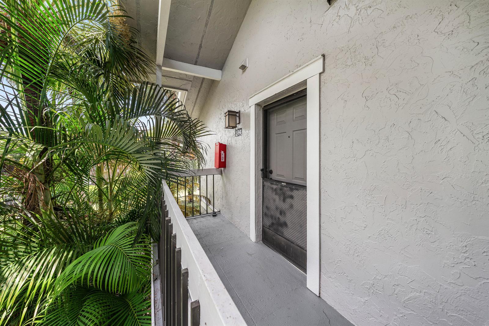 An exterior walkway features a grey door, a red fire extinguisher, and a palm tree — 11863 Wimbledon Circle # 504, Wellington FL 33414, WELLINGTON, FL