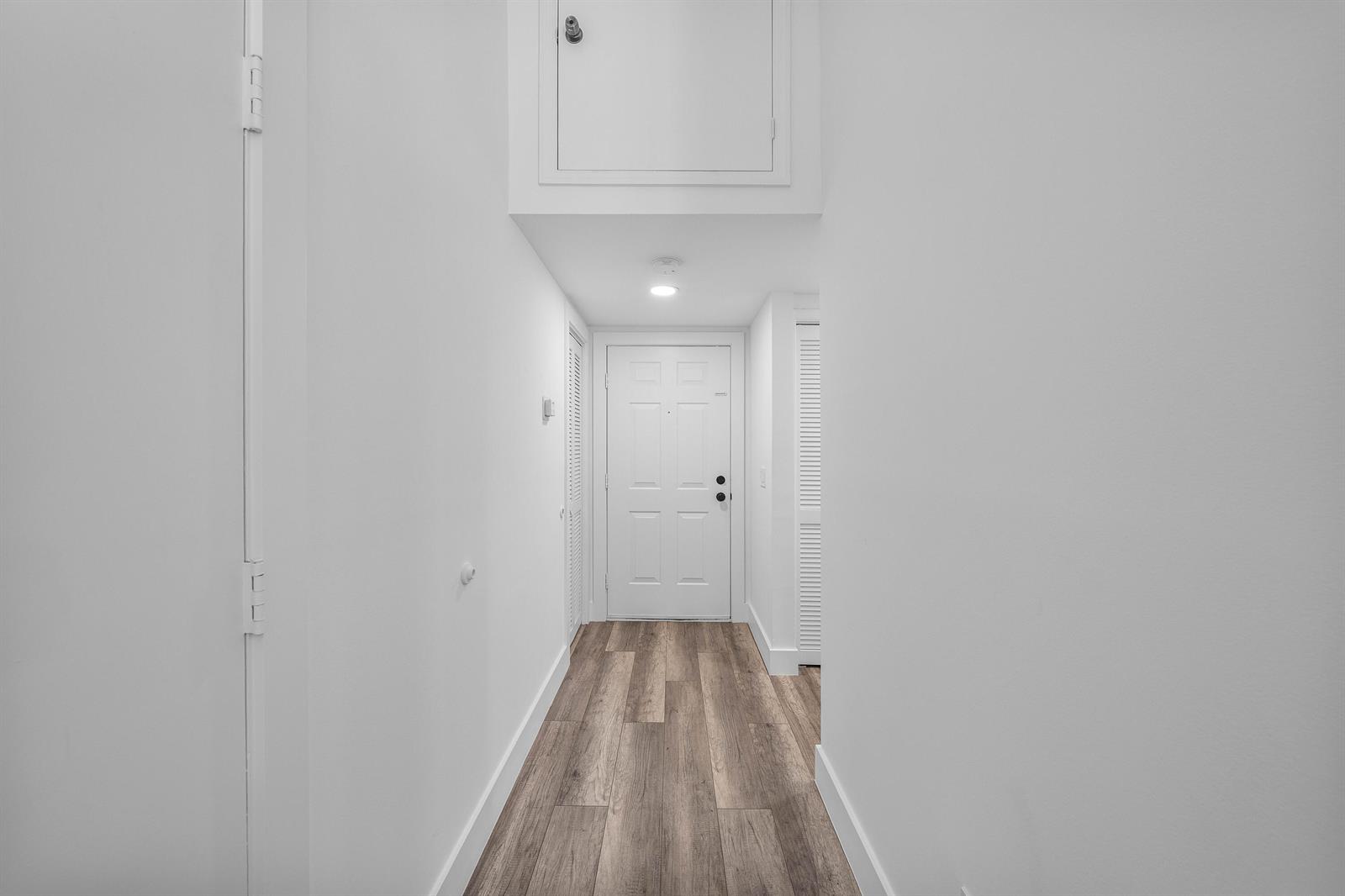 A hallway with white walls, wood-look flooring, and a white door at the end — 11863 Wimbledon Circle # 504, Wellington FL 33414, WELLINGTON, FL