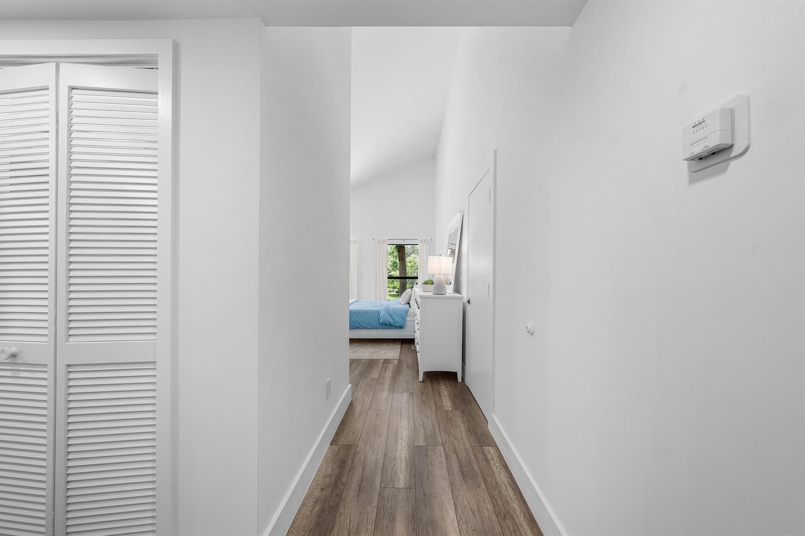 A hallway with wood-look flooring leads to a bedroom with a vaulted ceiling — 11863 Wimbledon Circle # 504, Wellington FL 33414, WELLINGTON, FL