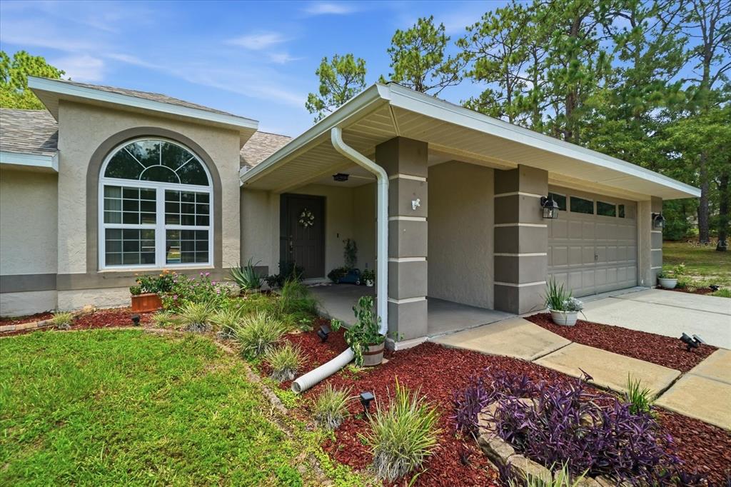 A single-story house exterior features a covered entryway, a two-car garage, and landscaped garden beds — 2877 W AXELWOOD DRIVE, BEVERLY HILLS, FL