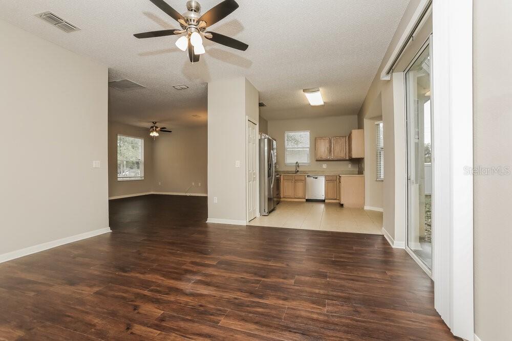 A view of a living room with wood-look floors leading into a tiled kitchen area — 233 BLUFF PASS DRIVE, EUSTIS, FL