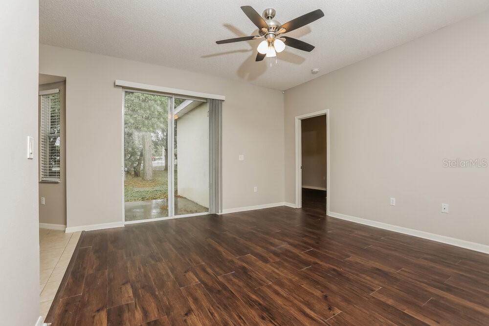 An empty room features dark wood-look flooring, a ceiling fan, and a sliding glass door — 233 BLUFF PASS DRIVE, EUSTIS, FL