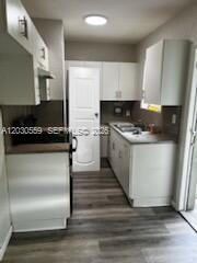 A kitchen with white cabinets, light wood-look flooring, and a white door — 1820 NW 127th St # 1820, Miami FL 33167, MIAMI, FL