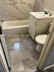 A bathroom features a white vanity, a toilet, and a bathtub with marble-patterned wall tiles — 1820 NW 127th St # 1820, Miami FL 33167, MIAMI, FL